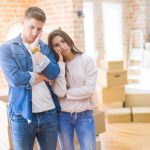 Couple moving in a house looking tired and depressed with crossed arms.