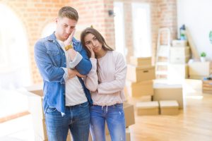 Couple moving in a house looking tired and depressed with crossed arms.