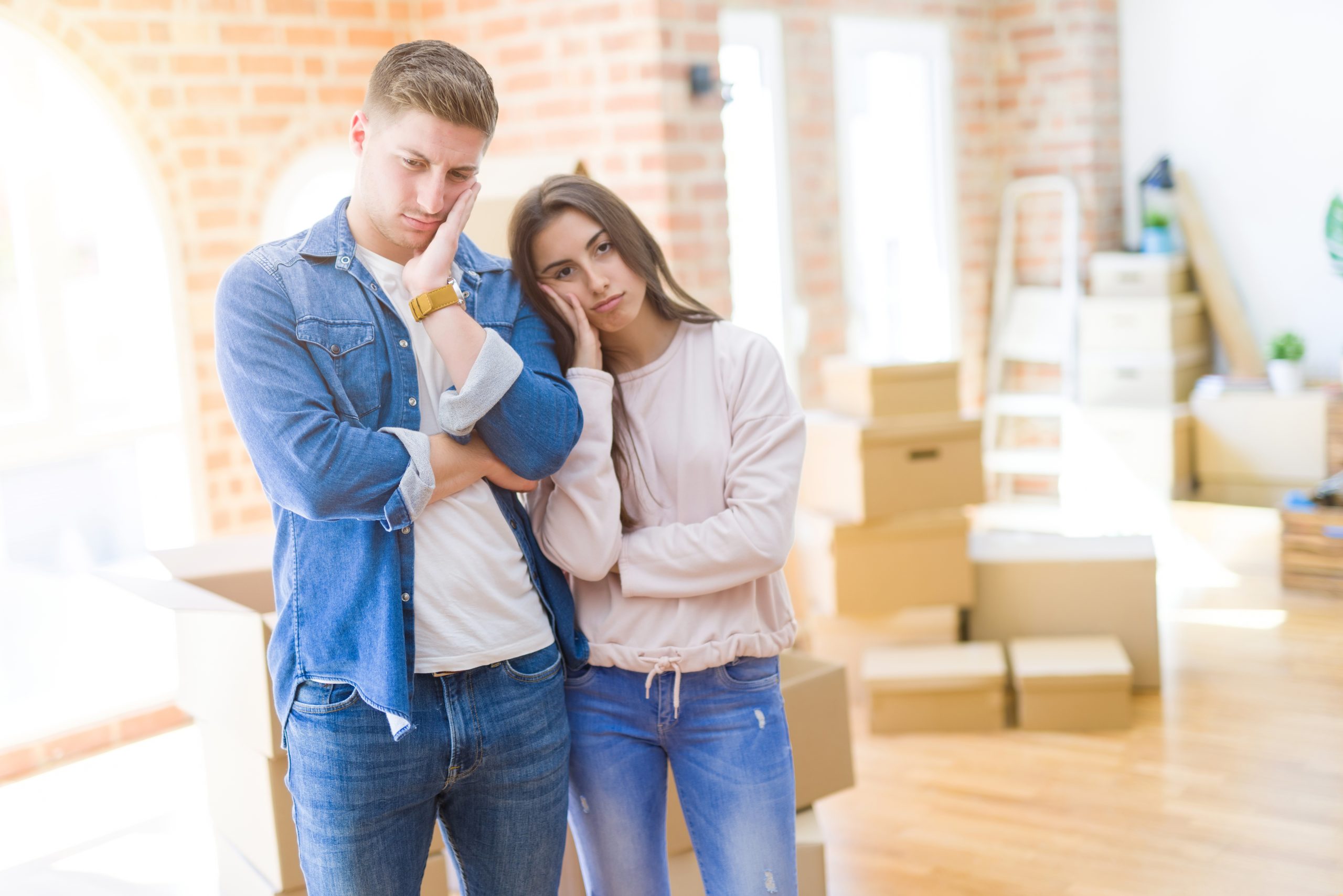 Couple moving in a house looking tired and depressed with crossed arms.
