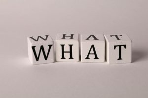 Four white wooden blocks on a light background spelling out the word "WHAT" in bold black letters, symbolizing curiosity or a frequently asked question.