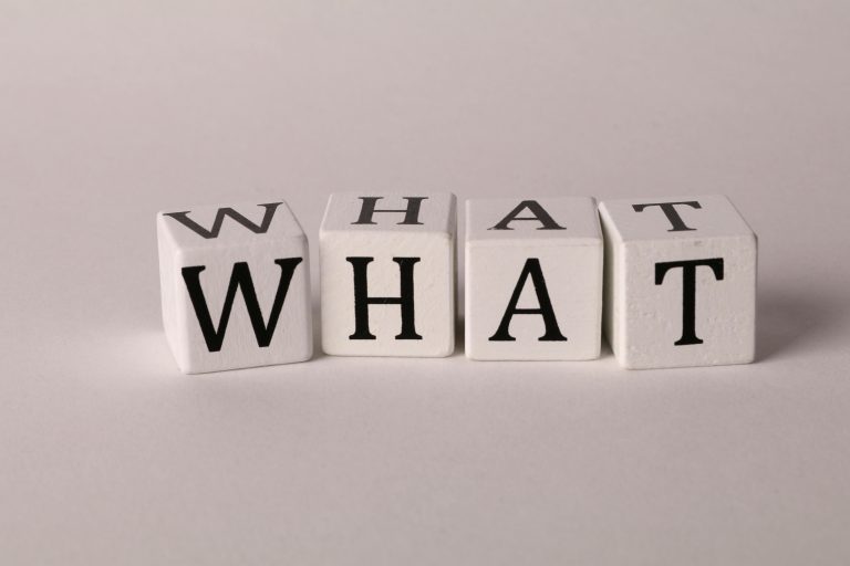 Four white wooden blocks on a light background spelling out the word "WHAT" in bold black letters, symbolizing curiosity or a frequently asked question.