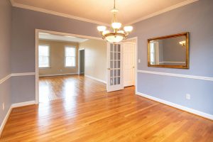 Bright empty dining room with hardwood floors, a gold-framed mirror, chandelier lighting, and a view into an adjacent living space, capturing the quiet stillness of a home ready for its next chapter.