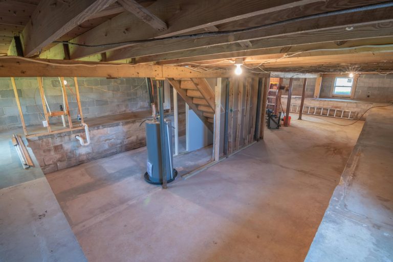 Unfinished basement with exposed concrete walls, wooden beams, and a water heater, illustrating potential hidden defects like water intrusion that may be discovered after purchasing a home.