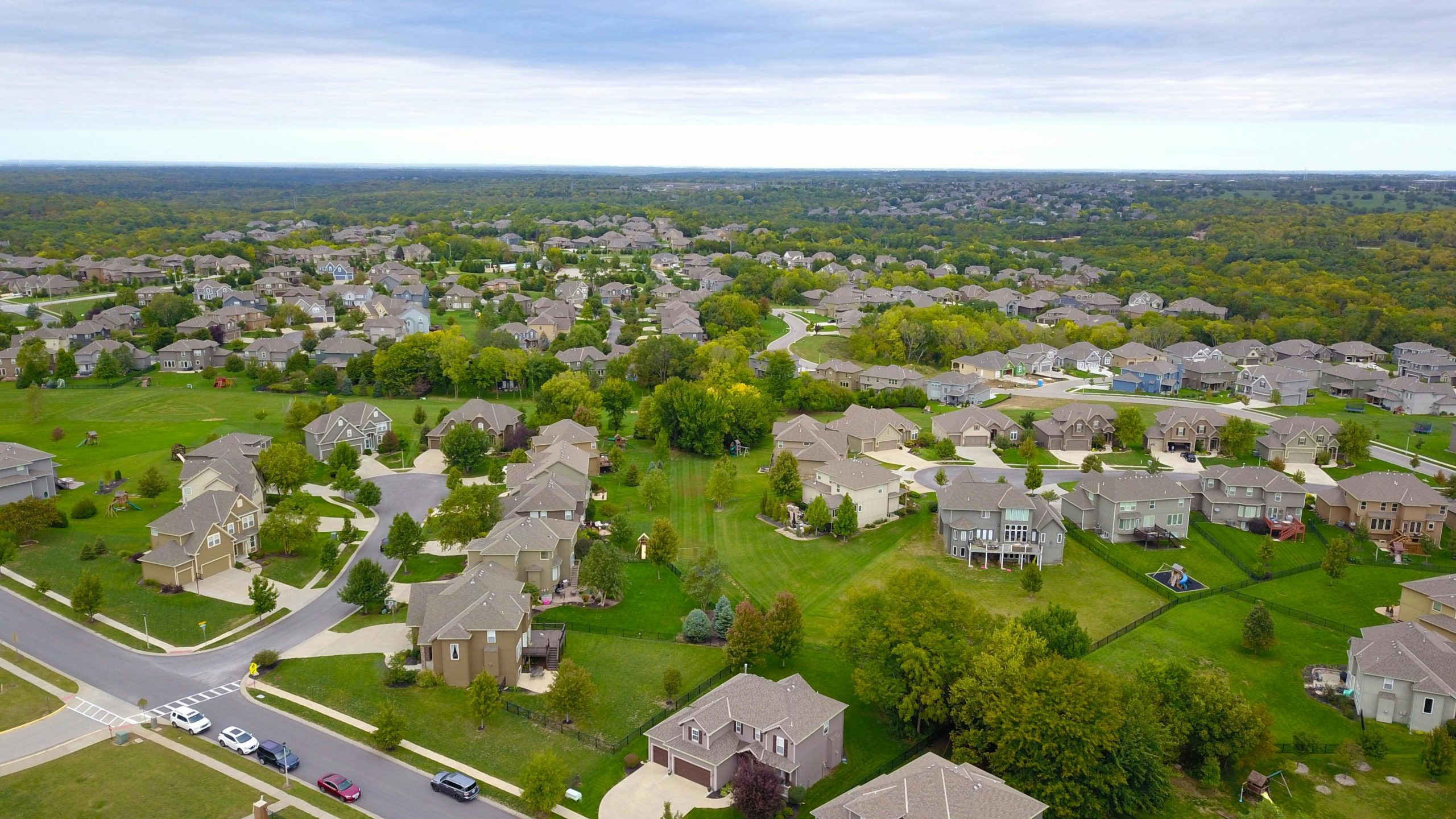 Aerial view of a large suburban neighborhood with rows of single family homes, green lawns, and tree-lined streets, representing growing housing inventory in the real estate market.
