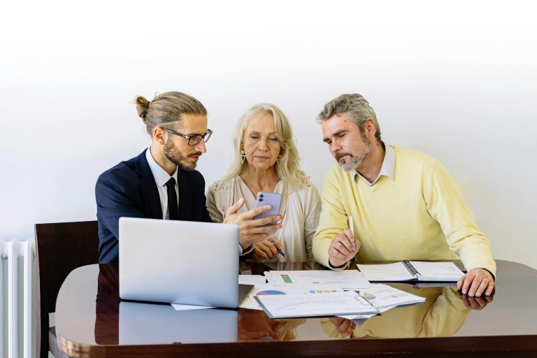 A real estate agent sitting with a couple showing them documents while his computer is open.