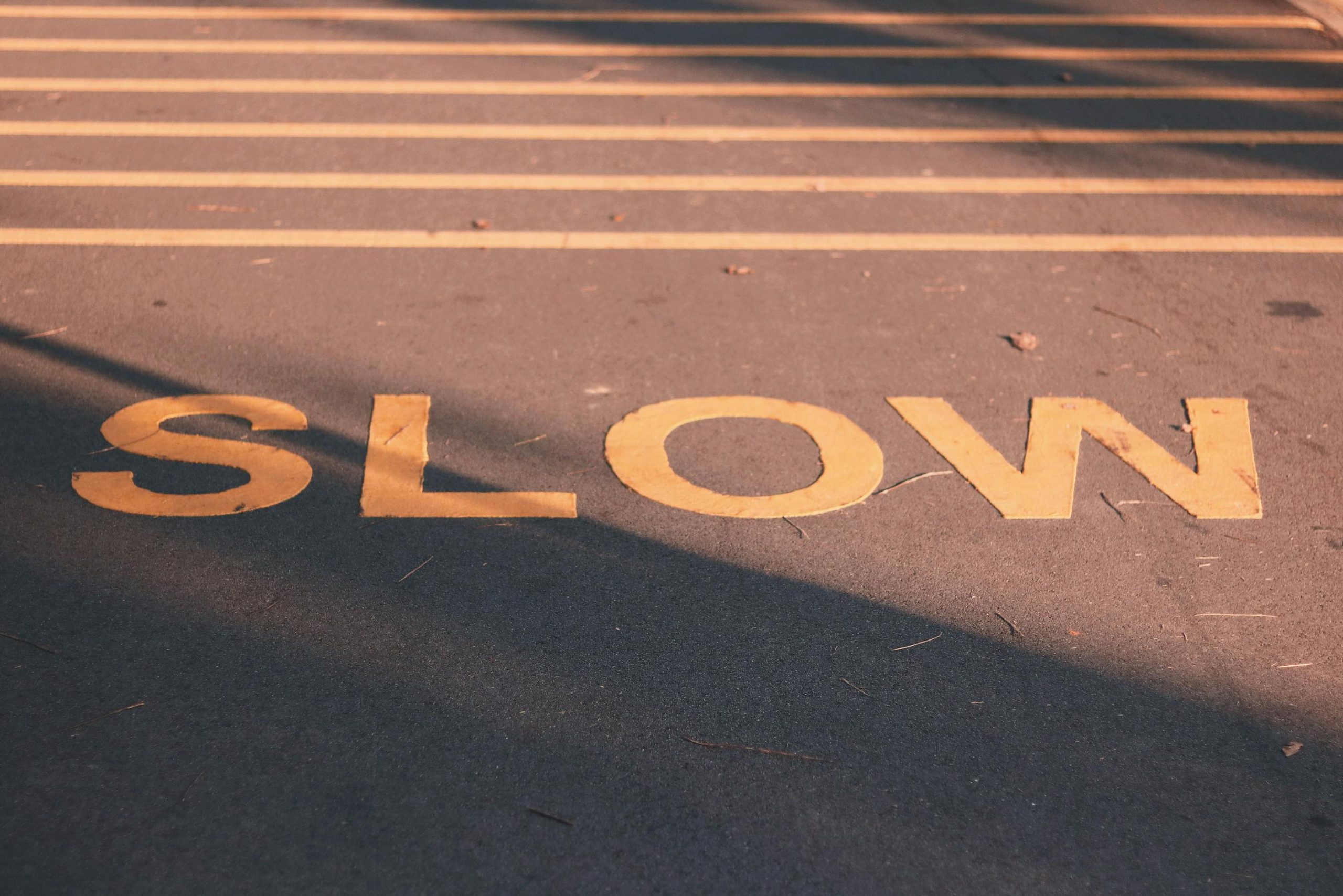 - Unbiased Real Estate Advice: The Truth About Real Estate Yellow painted word "SLOW" on asphalt, symbolizing the importance of pausing and reading real estate contracts carefully before signing.