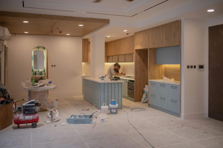 Two contractors working on a modern kitchen remodel with tools, paint, and materials spread across the floor, capturing a mid-renovation scene that reflects remodeling trends right now.