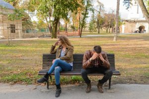 Couple sitting on a bench in a park looking stressed and unhappy.