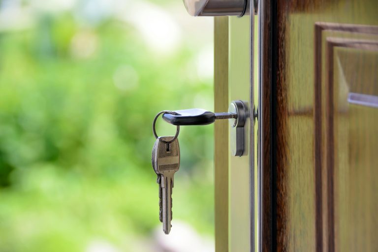 Close-up of a house key inserted into the front door lock with a lush green garden visible in the background.