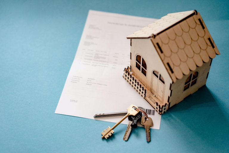 Miniature wooden house and house keys placed on top of legal paperwork, symbolizing a real estate deed and property ownership transfer.