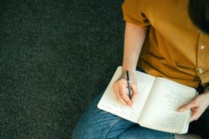 Homebuyer writing a checklist in a notebook, sitting on carpeted floor, creating a personal wish list for finding the right home.