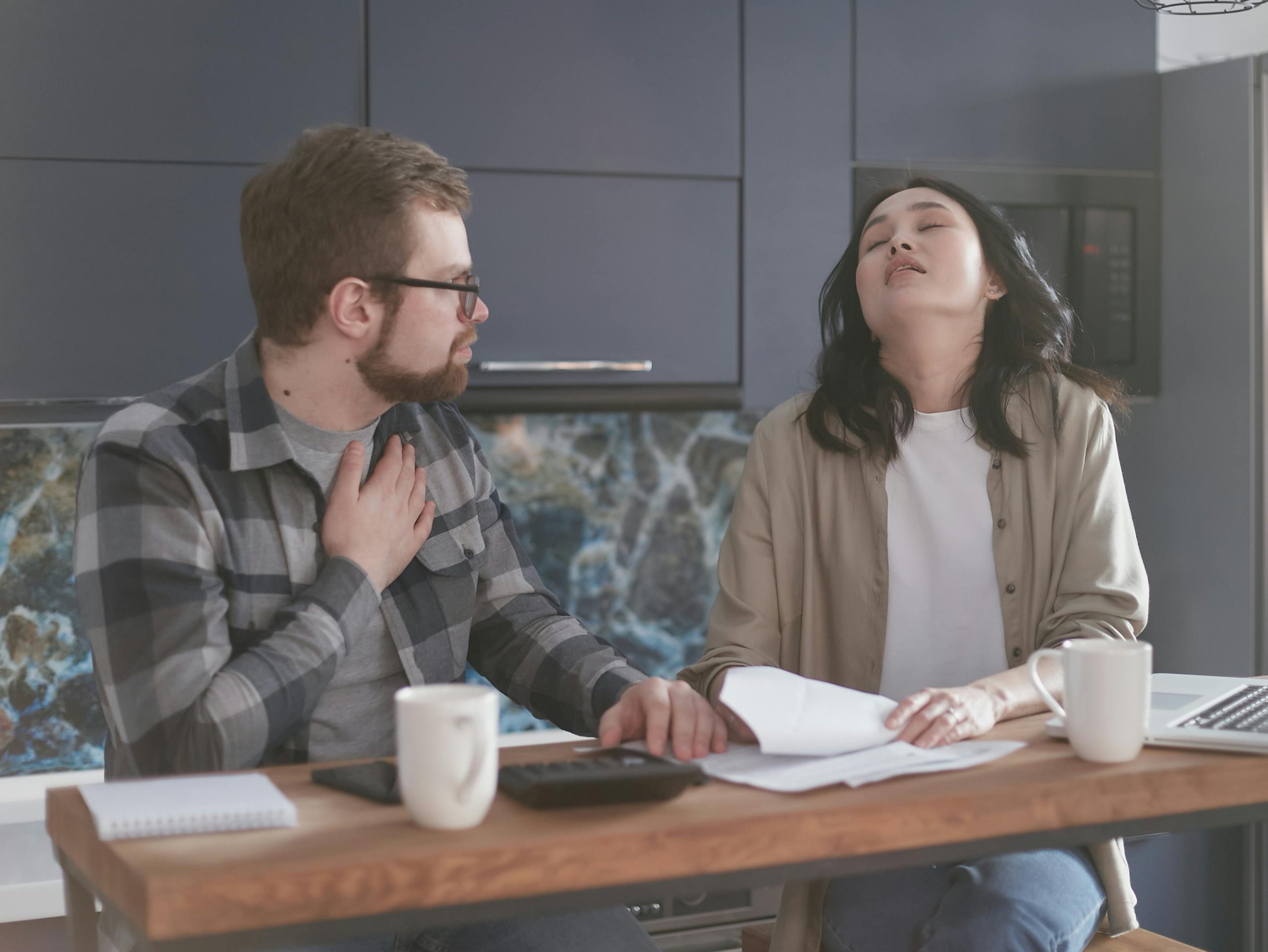 - Unbiased Real Estate Advice: The Truth About Real Estate Frustrated couple sitting at a kitchen table reviewing paperwork, capturing the stress and regret of hiring the wrong real estate agent without proper interviews.