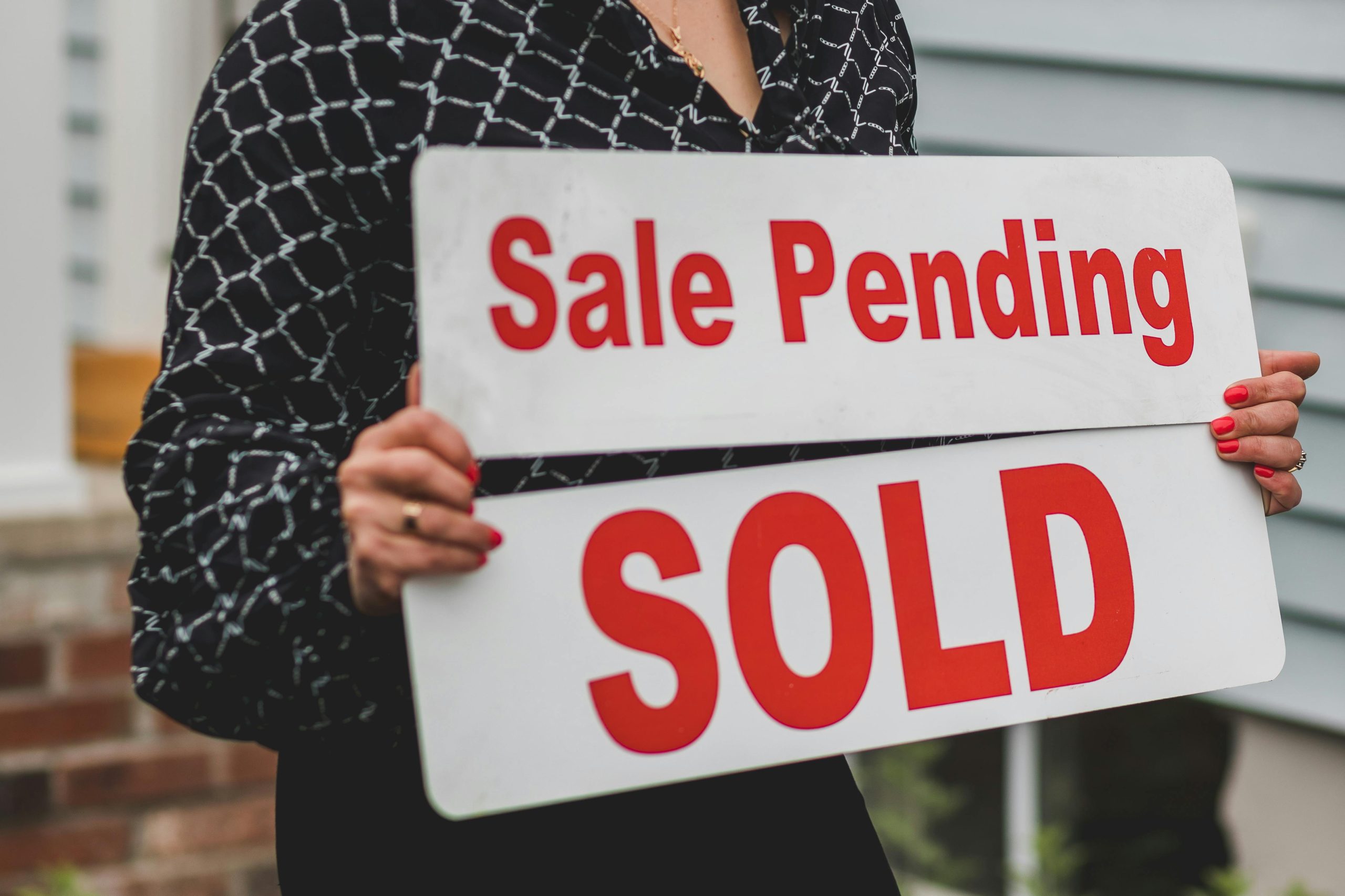 - Unbiased Real Estate Advice: The Truth About Real Estate A real estate agent holding a "Sale Pending" and "SOLD" sign in front of a house, symbolizing a home purchase in progress.
