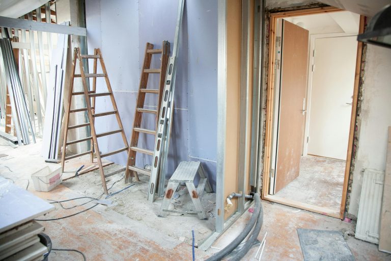 Basement under renovation with ladders, drywall, and construction materials scattered across the floor.