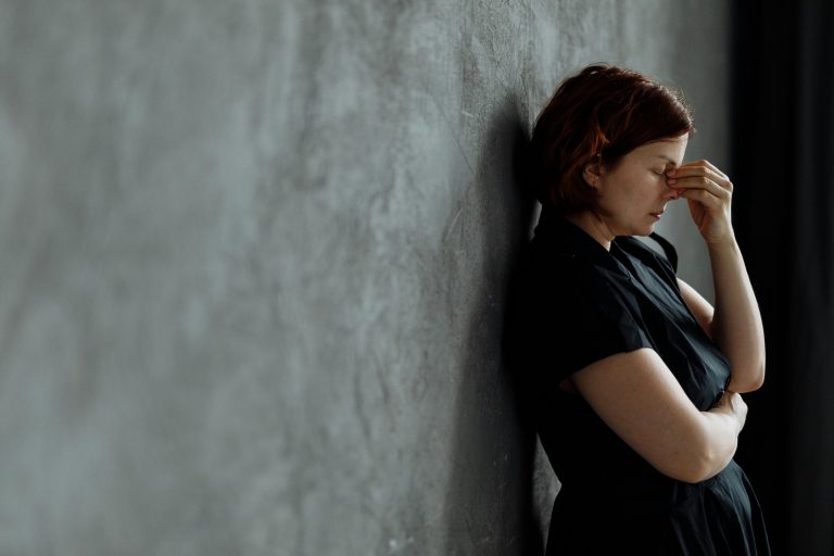 Frustrated woman leaning against a wall, holding her head in stress, symbolizing the emotional toll of difficult real estate negotiations.