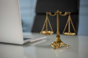 A brass scale of justice next to a laptop on a glass desk, symbolizing the legal support of a real estate attorney in property transactions