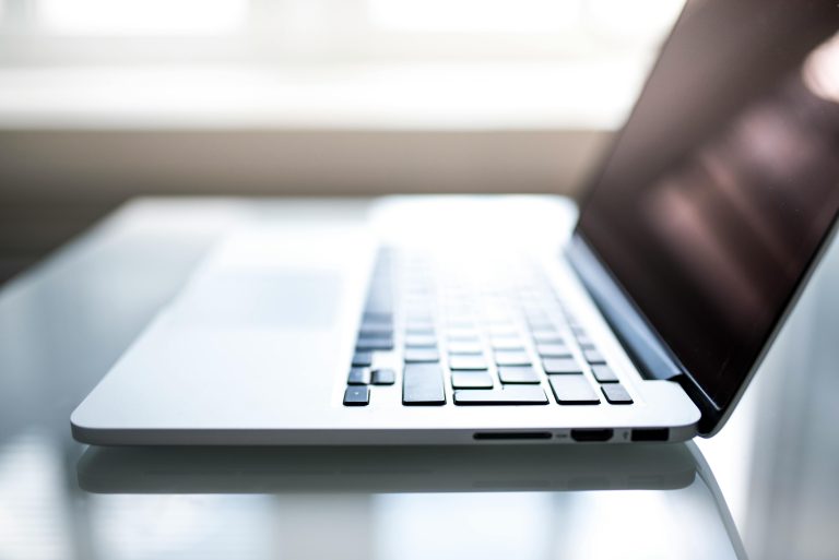 Close-up of a laptop computer on a glass table, symbolizing online real estate searches and the digital tools used in the MLS system