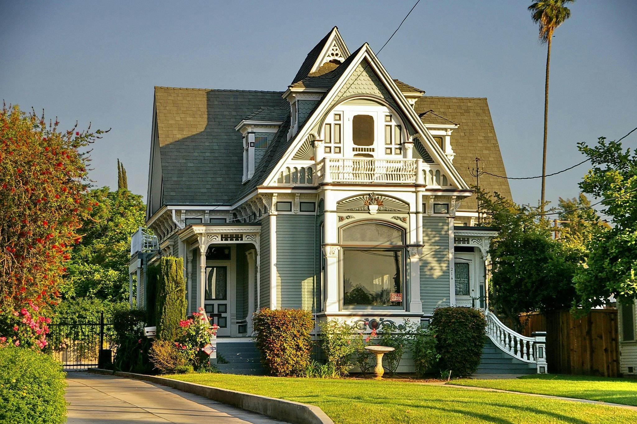 - Unbiased Real Estate Advice: The Truth About Real Estate Victorian-style historic home with ornate architectural details, steep gabled roof, and manicured lawn in a tree-lined neighborhood at sunset.