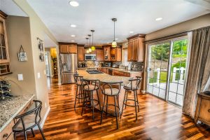 Spacious modern kitchen with wood cabinets, granite countertops, stainless steel appliances, and a large center island, opening to a backyard deck through glass sliding doors.