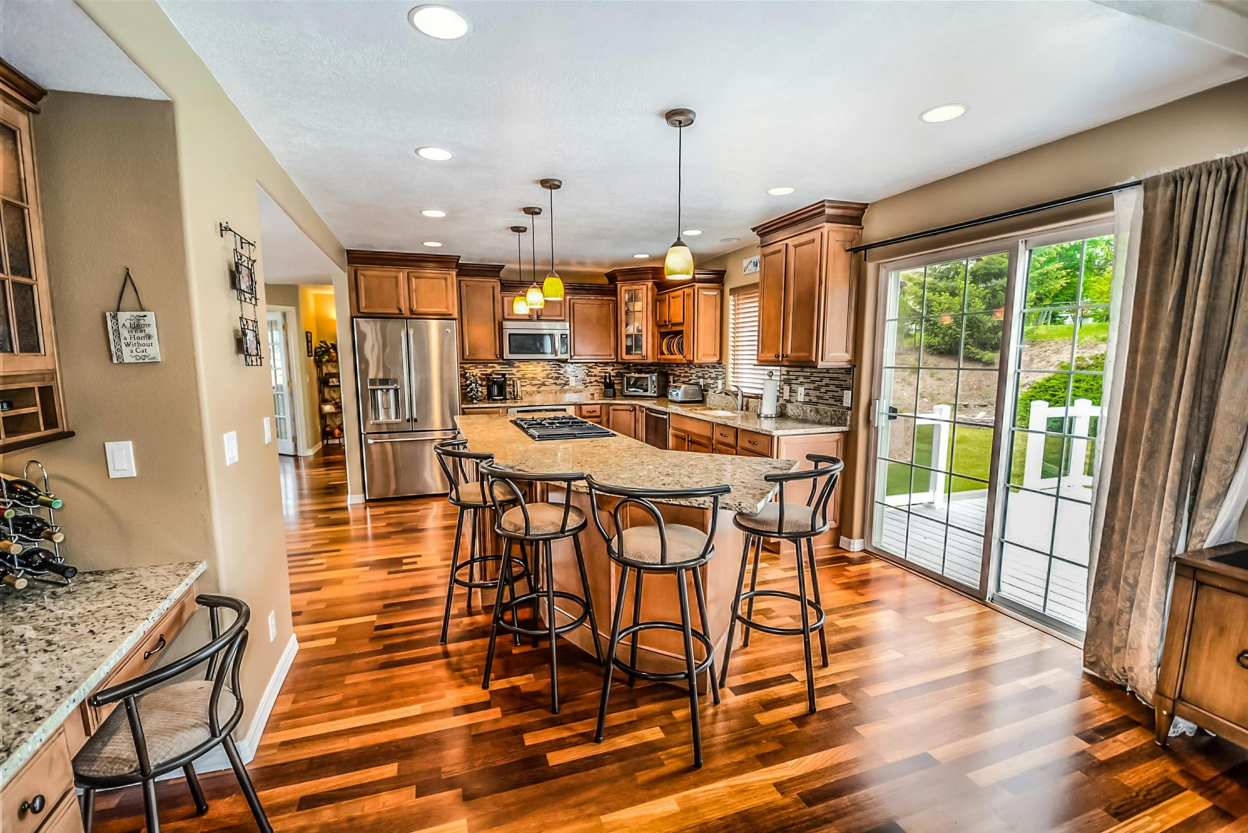 Spacious modern kitchen with wood cabinets, granite countertops, stainless steel appliances, and a large center island, opening to a backyard deck through glass sliding doors.