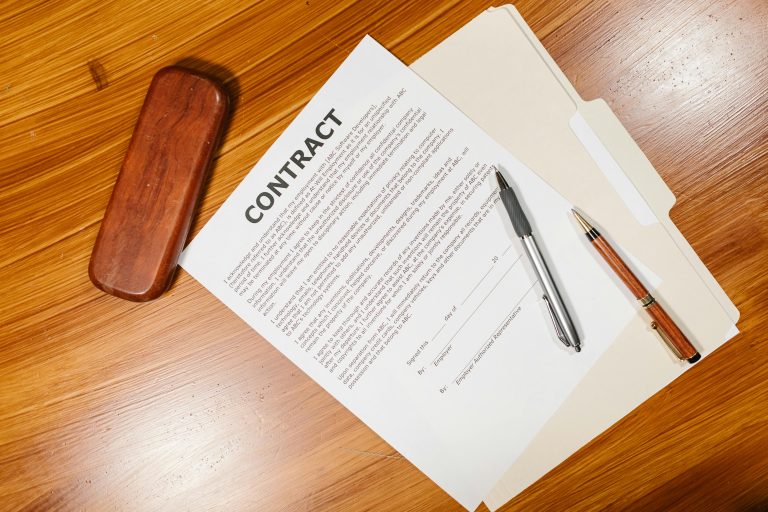 A close-up of a real estate contract with pens on a wooden desk, symbolizing the importance of written buyer agreements in real estate transactions.
