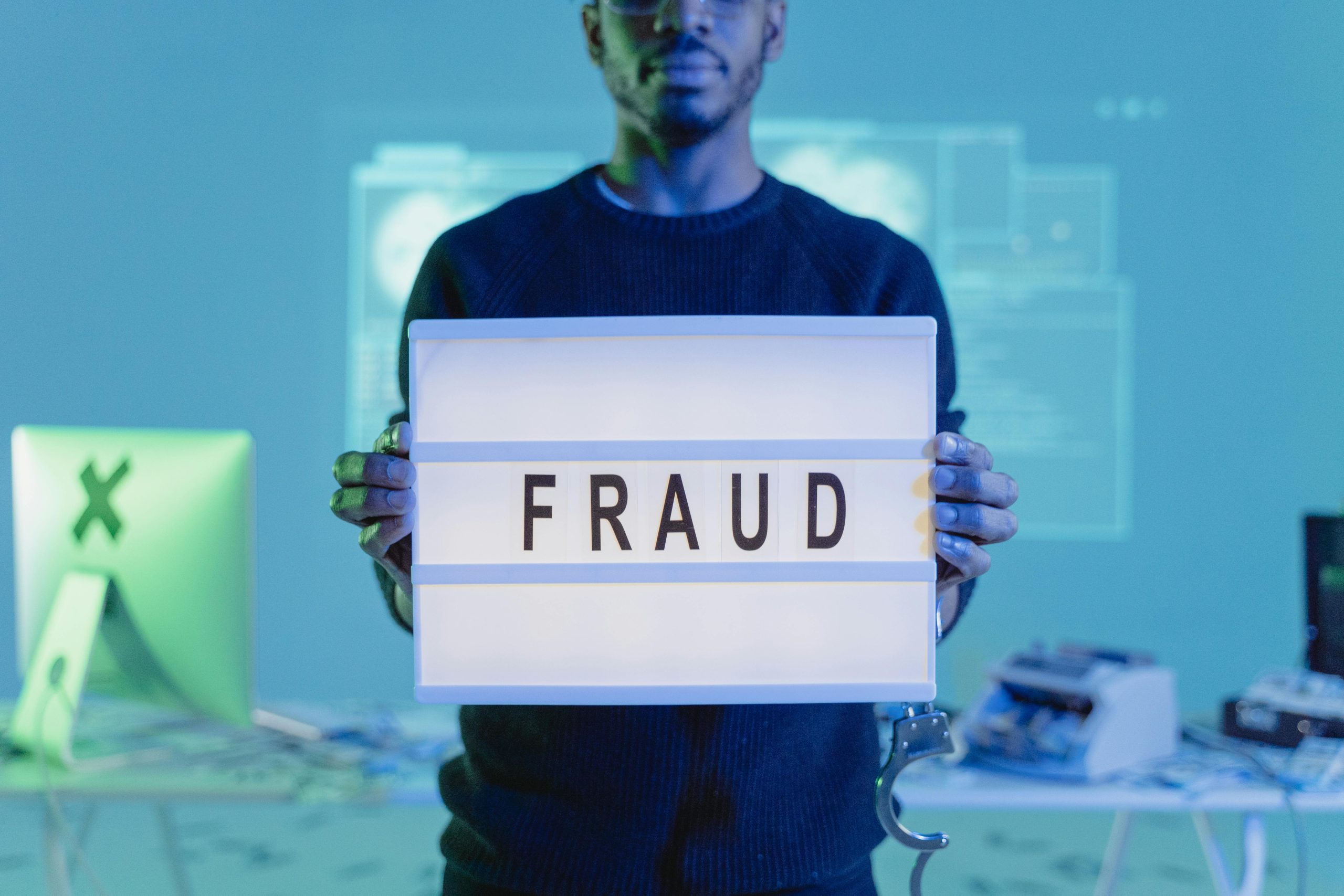Person holding a lightbox sign that says "FRAUD" in a tech-themed room, symbolizing the dangers of real estate scams