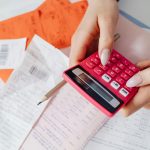 Person holding a pink calculator and pencil while reviewing receipts and financial documents, calculating expenses, budgeting, money management, seller concessions, home selling costs, financial planning, real estate transaction costs