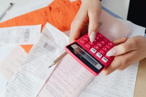 Person holding a pink calculator and pencil while reviewing receipts and financial documents, calculating expenses, budgeting, money management, seller concessions, home selling costs, financial planning, real estate transaction costs
