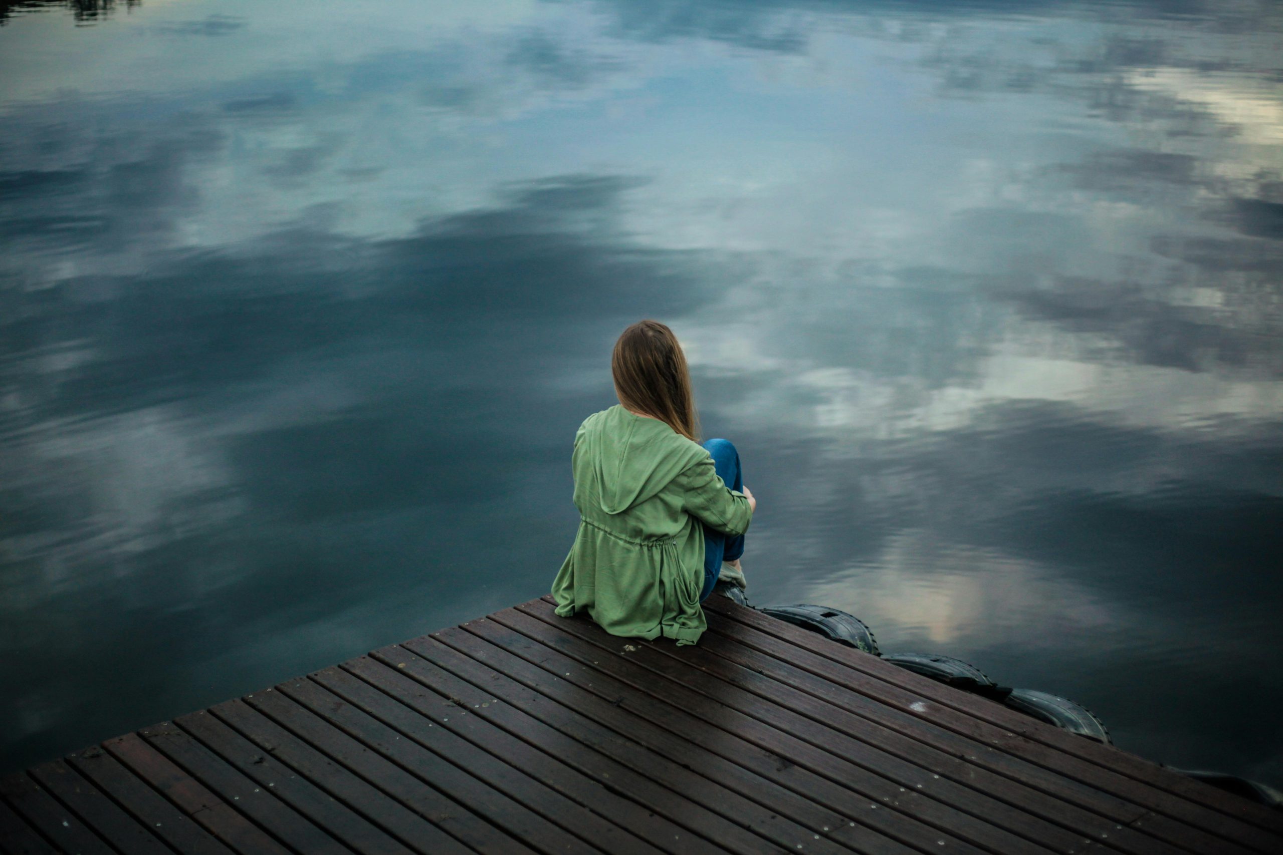 - Unbiased Real Estate Advice: The Truth About Real Estate A person sitting alone on a wooden dock looking out over calm water, symbolizing reflection and confusion after a seller accepts less than their offer.