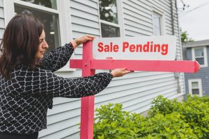 Real estate agent placing a "Sale Pending" sign in front of a house, indicating the property is under contract.