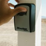 Close up of a hand entering a code on a lockbox mounted to a post, illustrating unsecured access risks and the need for supervised showings.