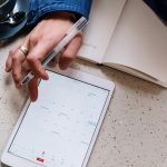Hand planning home showings on a tablet calendar next to an open notebook and coffee, scheduling the right showing notice for an occupied home.