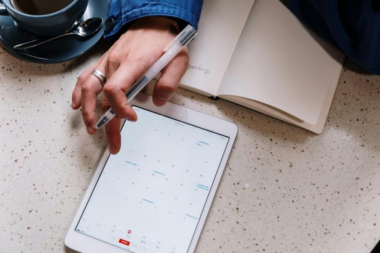Hand planning home showings on a tablet calendar next to an open notebook and coffee, scheduling the right showing notice for an occupied home.
