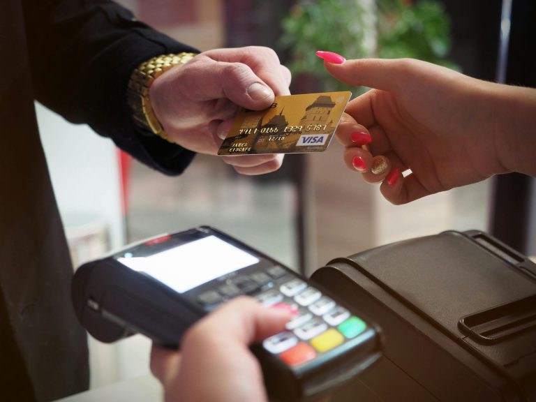 Close up of a person handing over a credit card to pay at a payment terminal representing hourly versus commission real estate agent fees.