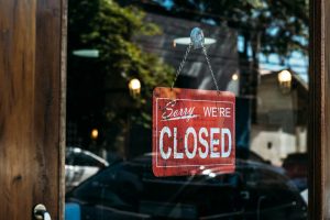 Red Sorry We Are Closed sign hanging on a glass door with street reflections, symbolizing a government shutdown and potential delays to real estate closings.