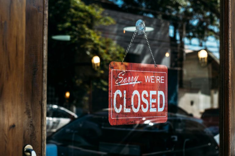 Red Sorry We Are Closed sign hanging on a glass door with street reflections, symbolizing a government shutdown and potential delays to real estate closings.