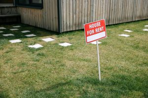 Red and white “House for Rent” sign placed in the front yard of a rental property.