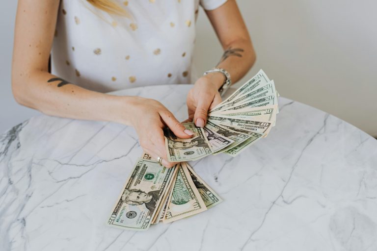 Hands counting a fan of U.S. dollar bills on a marble table representing money decisions in a home purchase and counter offer negotiations.