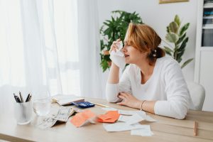 Woman sitting at a desk stressed over bills and finances with receipts, cash, and a calculator in front of her.