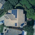 Aerial view of a suburban home with rooftop solar panels and mature trees, illustrating energy efficiency features that appeal to today’s buyers.