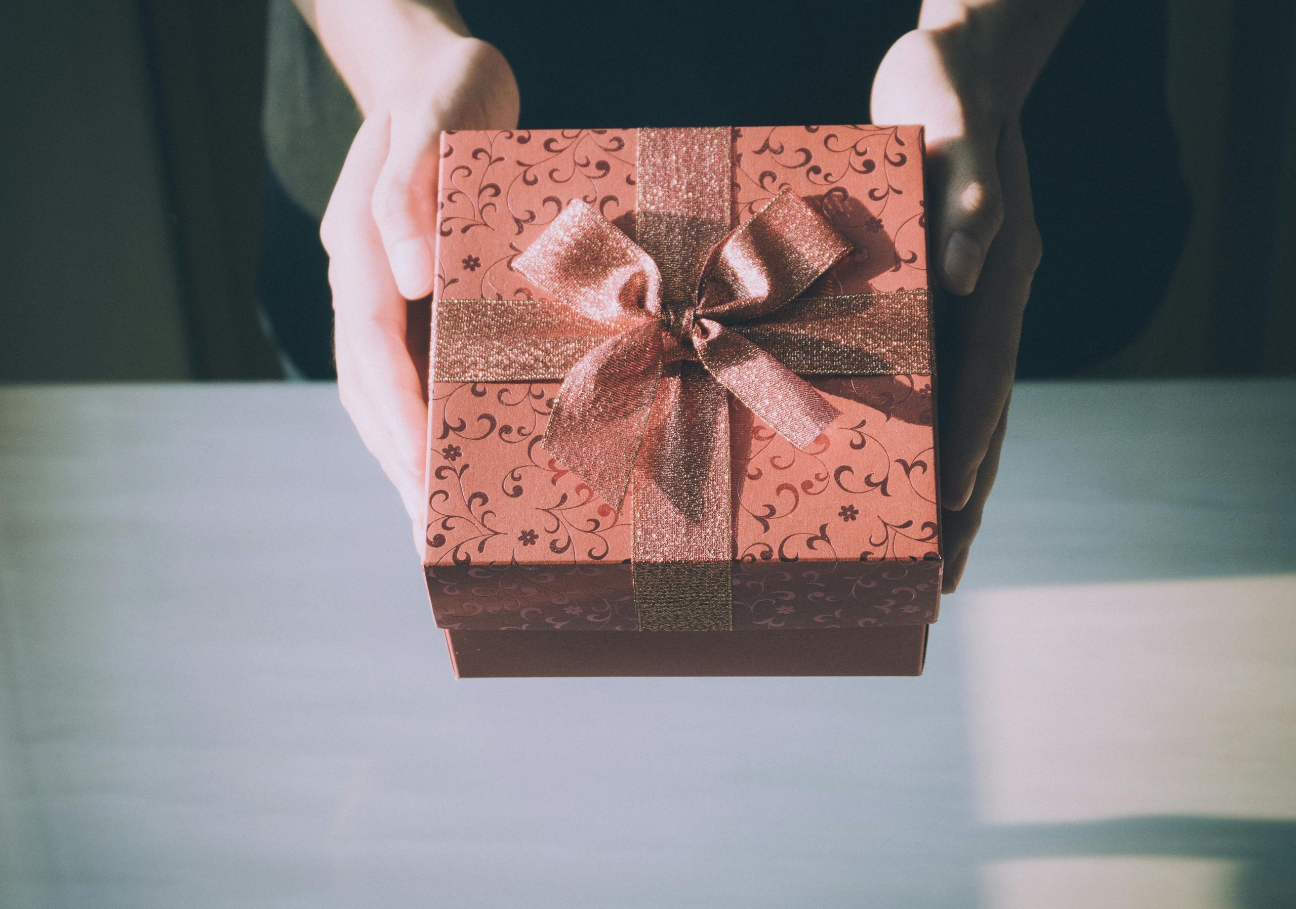 Hands holding a beautifully wrapped gift box with a bow, symbolizing the idea of a closing gift in real estate.