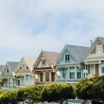 Row of colorful Victorian houses lined along a city street with trees.