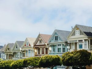 Row of colorful Victorian houses lined along a city street with trees.