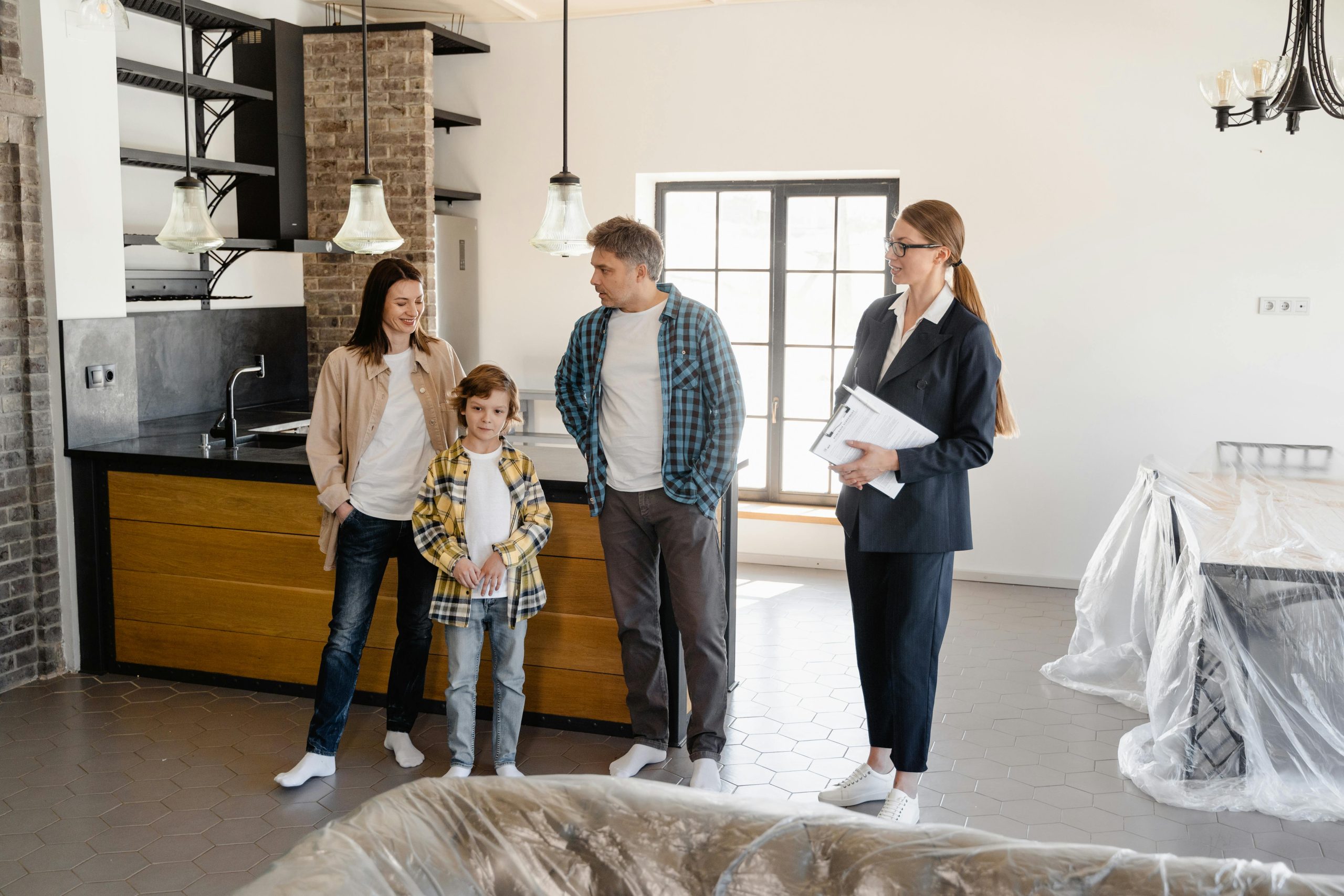 - Unbiased Real Estate Advice: The Truth About Real Estate Real estate agent guiding a family during a home showing in a bright kitchen and dining area with protective covers and natural light.