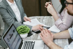 Home buyers meet with a loan officer at a table reviewing mortgage paperwork and laptops while discussing switching lenders before closing.