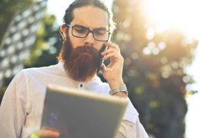Bearded homeowner on the phone checking a tablet in bright sunlight after discovering home showing requests went to the junk folder.