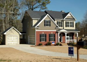 Front view of a newly sold suburban house with a driveway and a for sale sign still posted in the front yard.